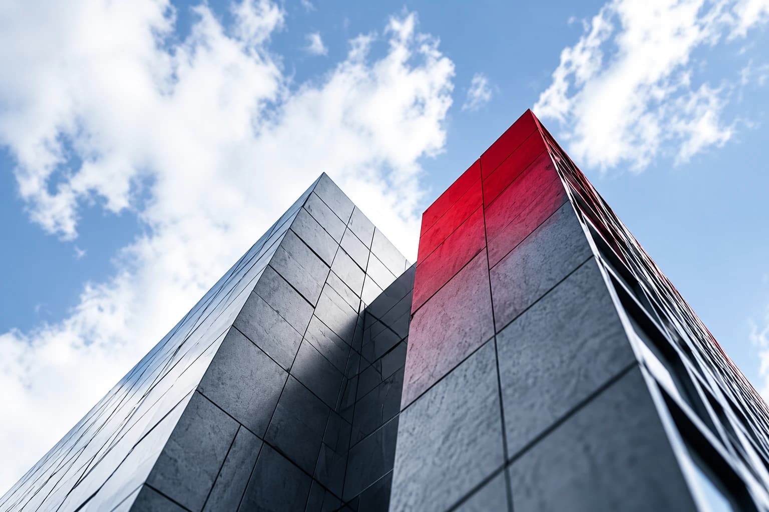 Two tall modern towers, one with a red accent, rising into a cloudy sky